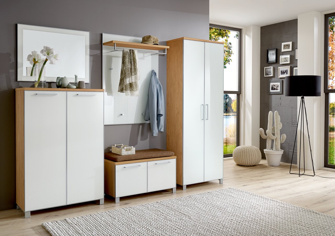 Modernes Garderoben-Set in heller Holzoptik mit weißen Hochglanzfronten, bestehend aus Schrank, Sitzbank und Wandpaneel mit Haken, aus der Perspektive eines hellen, geräumigen Zimmers mit großen Fenstern.