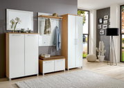 Moderne garderobeset in een lichte houtlook met witte hoogglansfronten, bestaande uit een kast, een bankje en een wandpaneel met haken, gezien vanuit een lichte, ruime kamer met grote ramen.