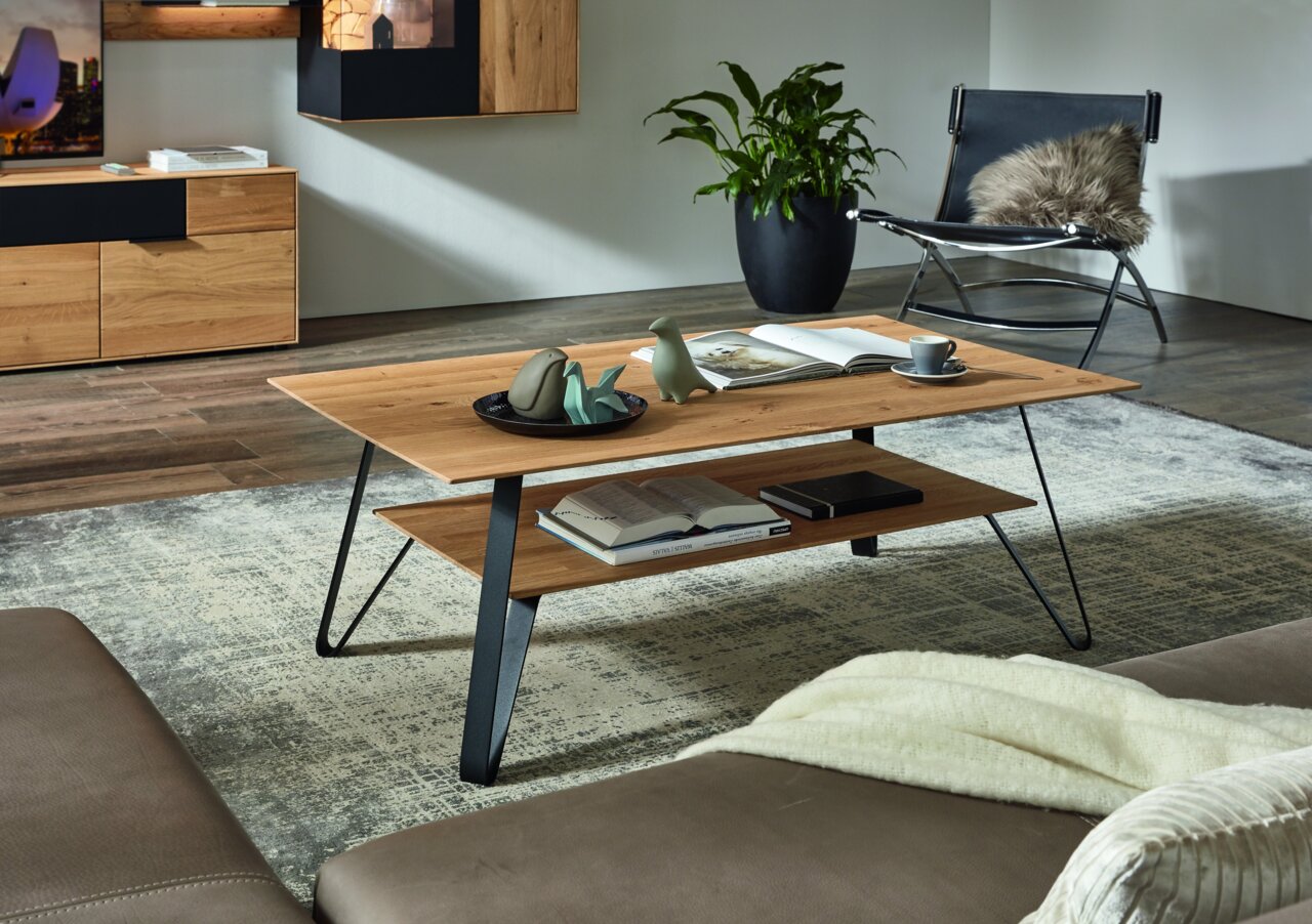 Moderner Couchtisch aus Holz mit schwarzem Metallgestell, dekoriert mit Büchern und Keramikfiguren, in einem stilvollen Wohnzimmer. Perspektive von der Seite.