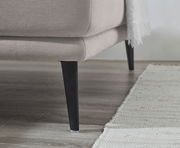 Nahaufnahme einer Rundecke (L) mit hellgrauem Stoffbezug und schwarzen, schlanken Beinen auf einem Holzboden, seitliche Perspektive.