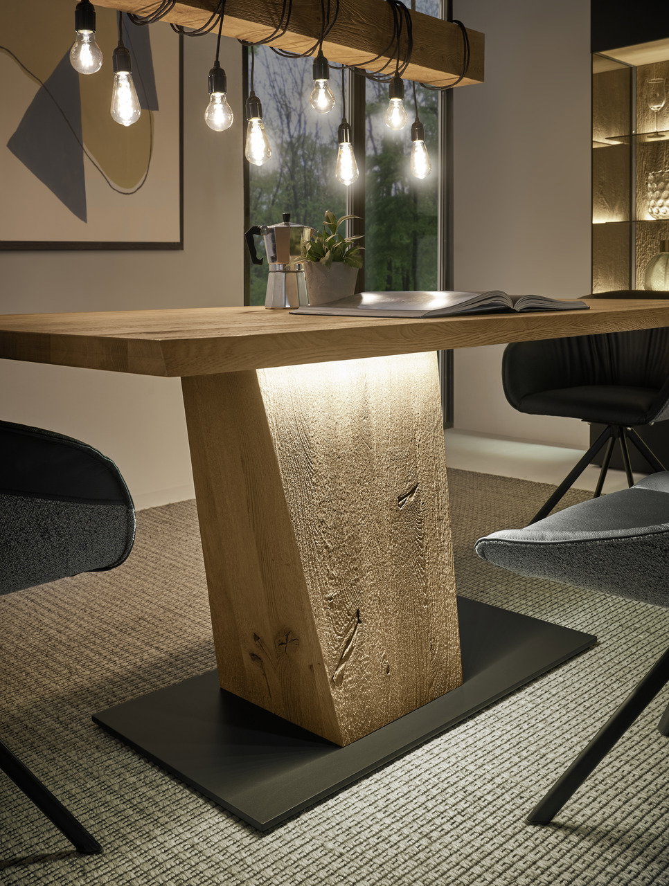 Moderner Esstisch aus Holz mit zentralem Sockel, umgeben von stilvollen Stühlen, aus der seitlichen Perspektive betrachtet.