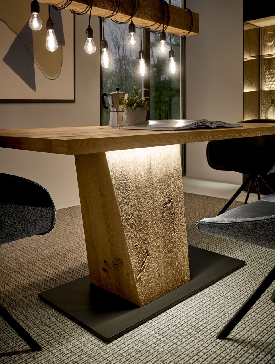 Moderne houten eettafel met een centrale voet, omringd door stijlvolle stoelen, gezien vanuit de zijkant.
