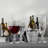 Vier elegante Gläser aus klarem Glas, darunter ein Weinkelch mit rotem Wein, ein kleinerer Weinkelch, ein Becher und ein Sektkelch, auf einem Tisch mit unscharfem Hintergrund von Weinflaschen. Frontale Perspektive.