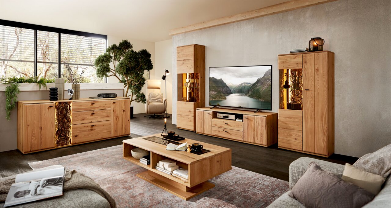 Wohnzimmer-Set aus massivem Holz mit Sideboard, TV-Lowboard, zwei Vitrinen mit warm beleuchteten Akzenten und Couchtisch, frontal in einer modernen Wohnraum-Szene fotografiert.