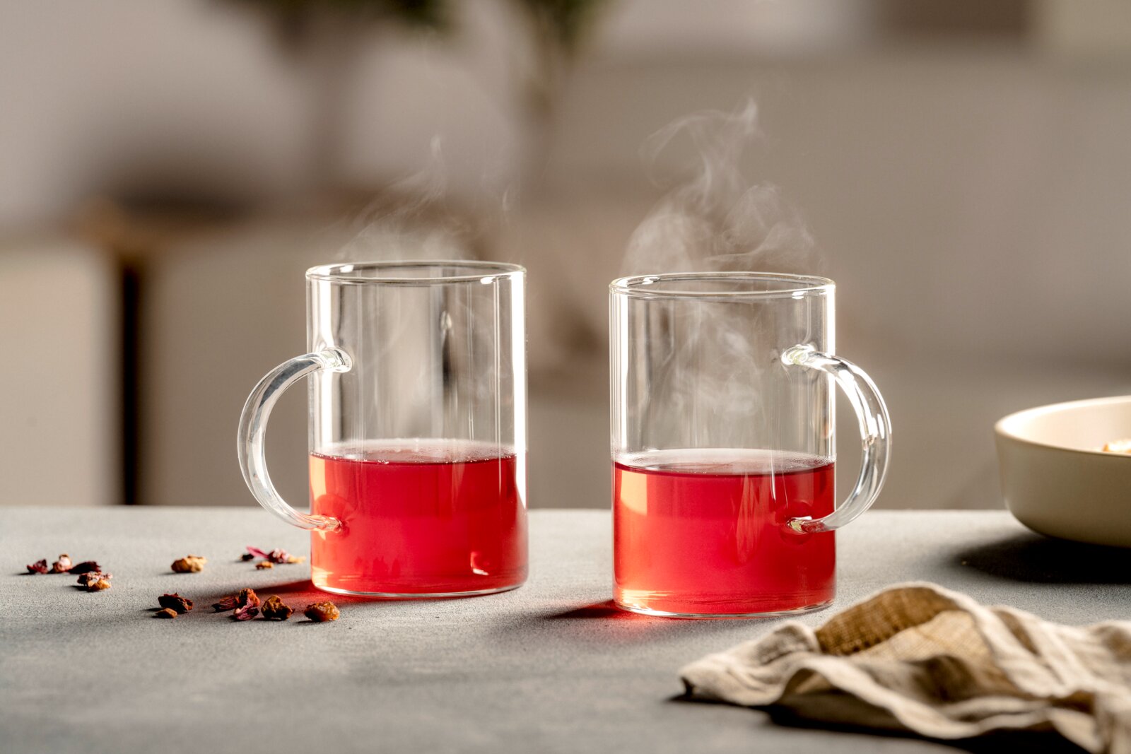 Leonardo Teegläser 2-tlg. SPECIAL Zwei transparente Glasbecher mit Henkeln und dampfendem rotem Tee, frontal in stimmungsvoller Tischszene betrachtet