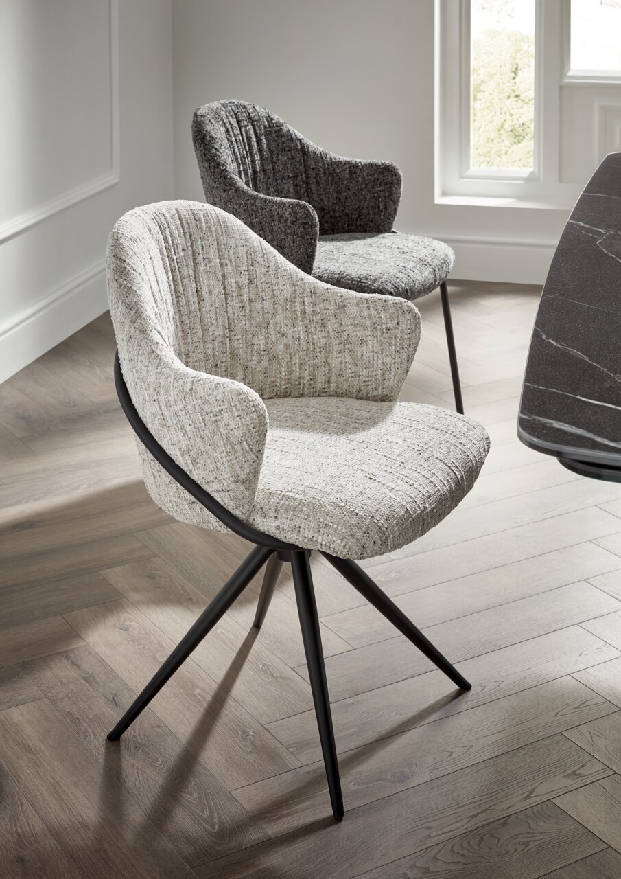 Zwei moderne Armlehnstühle mit Stoffbezug in hellen und dunklen Grautönen, auf einem Holzfußboden in einem hellen Raum, aus seitlicher Perspektive fotografiert.