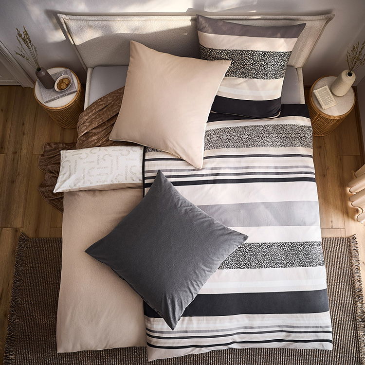 Modernes Bett mit gestreifter Bettwäsche in Grau- und Beigetönen, dekoriert mit mehreren Kissen