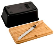 Schwarze Brotbox mit integriertem Messer, abgebildet aus der Vogelperspektive. Der Deckel der Box liegt umgedreht neben einem Holzbrett mit einem Brotmesser darauf.