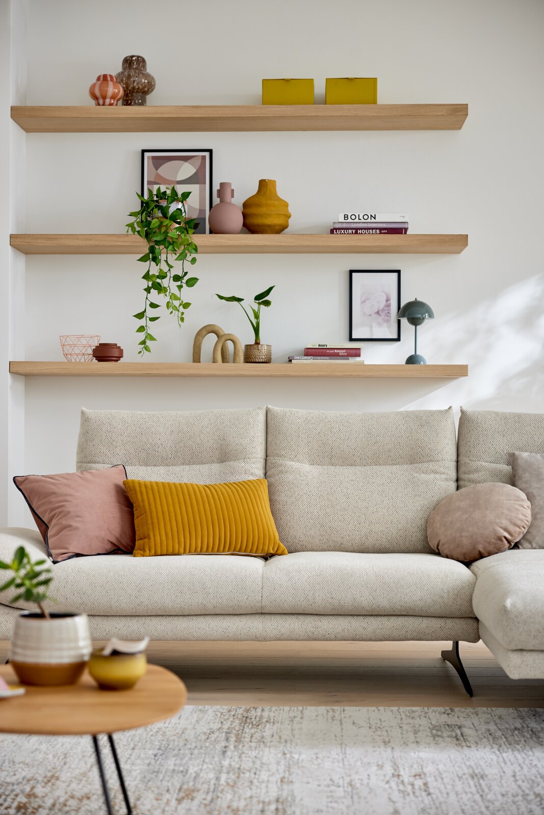 Vooraanzicht van een moderne longchair-combinatie van Musterring, model MR 2795, in een lichte woonkamer met decoratieve planken op de achtergrond.
