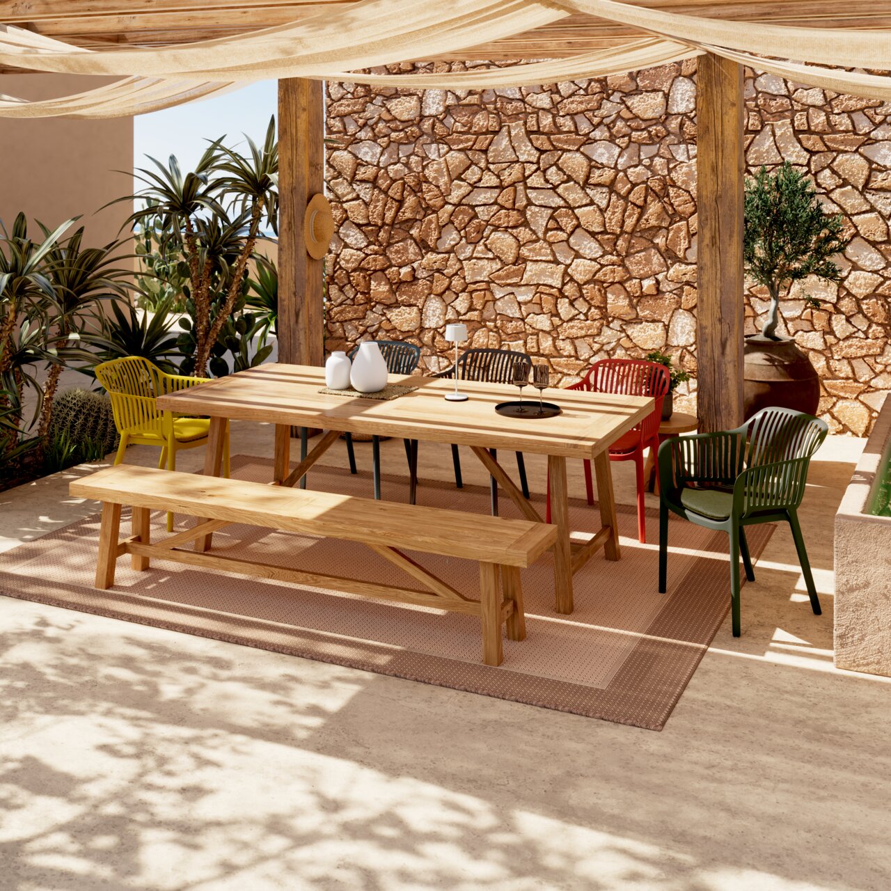 Een uitnodigende buitenopstelling met een houten tafel, omringd door kleurrijke stapelstoelen in rood, groen en geel. Het perspectief toont de stoelen van opzij, onder een schaduwrijke zonwering.