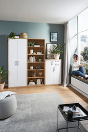 Wohnzimmer mit einem weißen Kleiderschrank, einem offenen Holzregal und einer weißen Kommode, seitliche Perspektive