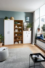 Wohnzimmer mit einem weißen Kleiderschrank, einem offenen Holzregal und einer weißen Kommode, seitliche Perspektive