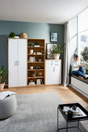 Wohnzimmer mit einem weißen Kleiderschrank, einem offenen Holzregal und einer weißen Kommode, seitliche Perspektive