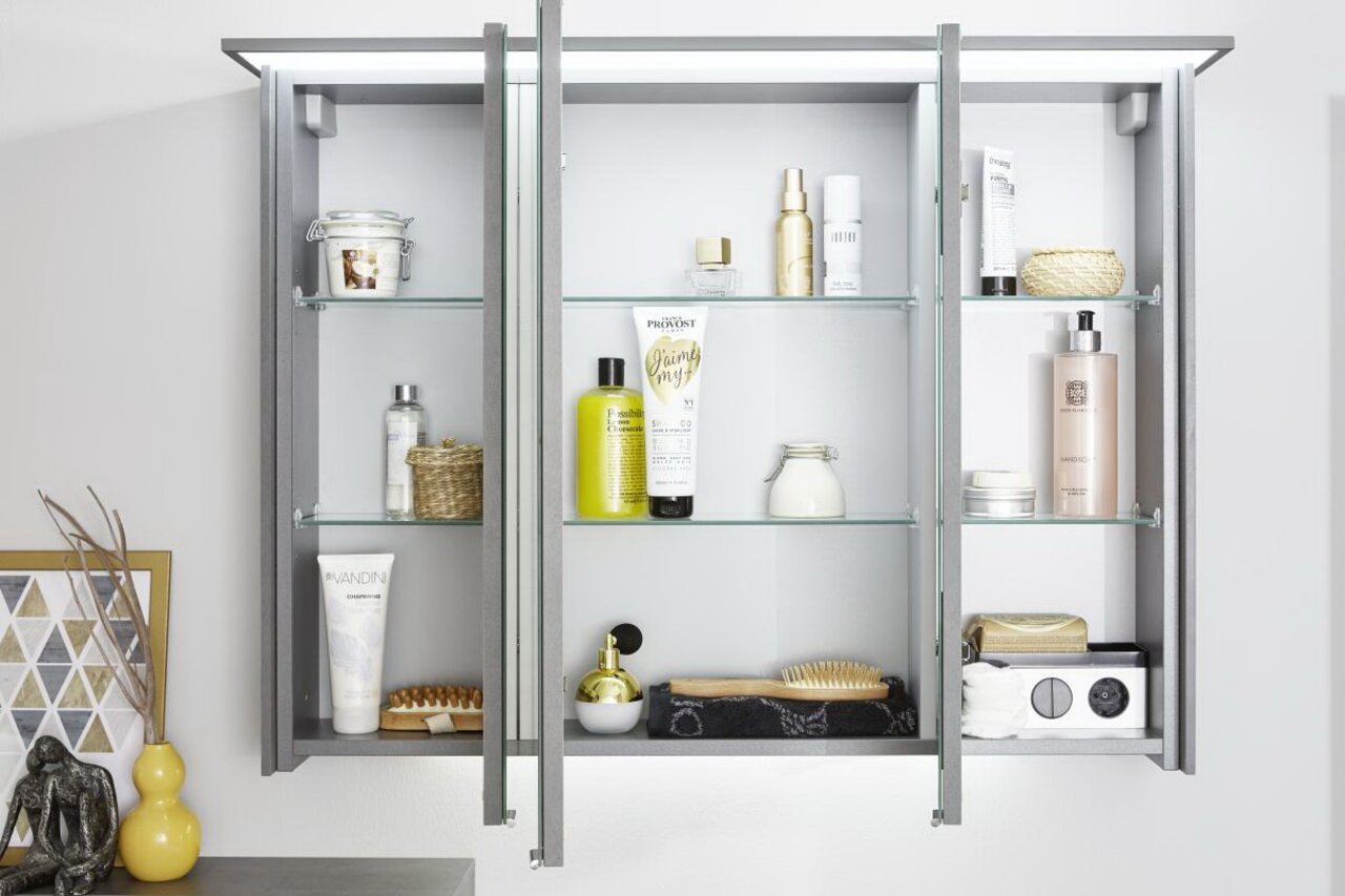 Moderne badkamercombinatie met drie spiegeldeuren, gevuld met verzorgingsproducten en accessoires, gezien van voren.