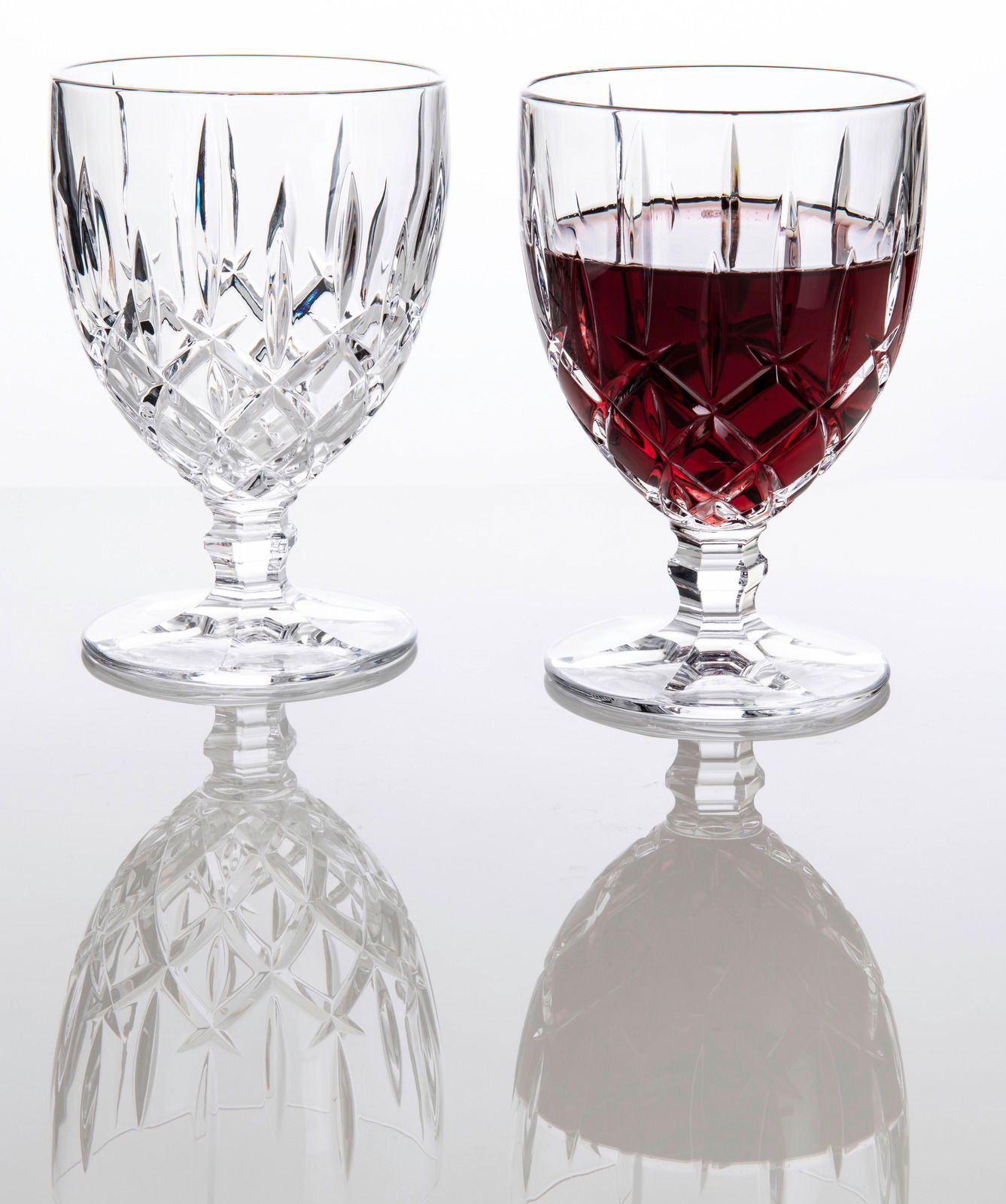 Zwei Weinkelche Noblesse 350ml, einer leer und einer mit Rotwein gefüllt, auf einer reflektierenden Oberfläche, seitliche Perspektive.