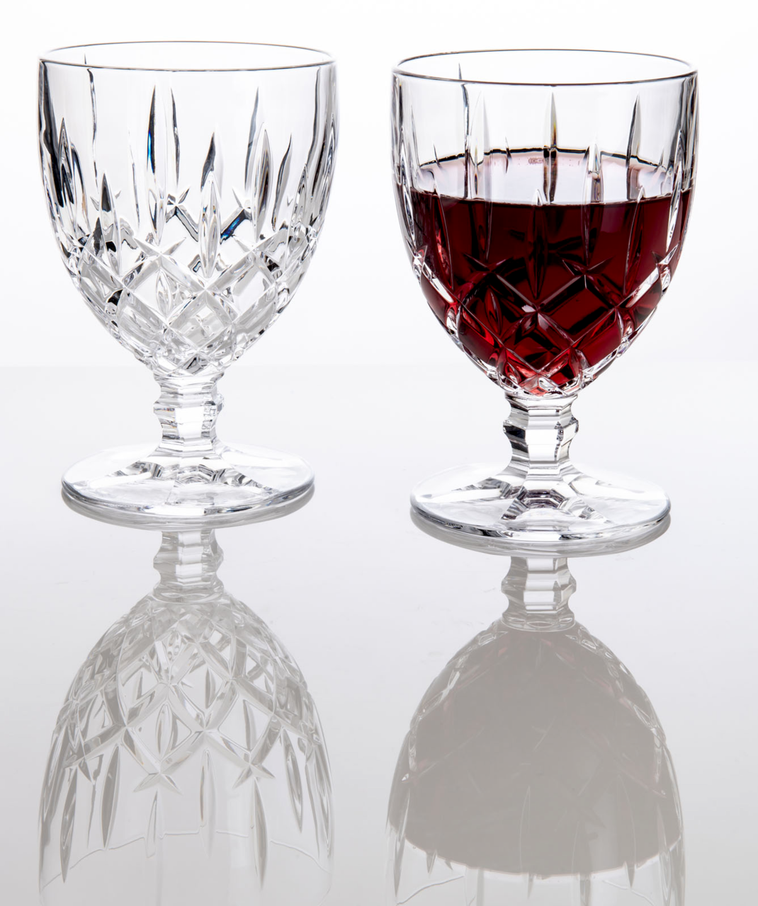Zwei Weinkelche Noblesse 350ml, einer leer und einer mit Rotwein gefüllt, auf einer reflektierenden Oberfläche, seitliche Perspektive.