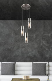 Moderne Hängeleuchte mit drei zylindrischen Lampenschirmen aus Metall und Glas, von der Decke hängend, in einem stilvollen Wohnzimmer mit grauer Wand und weißem Sofa. Perspektive von vorne.