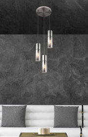 Moderne Hängeleuchte mit drei zylindrischen Lampenschirmen aus Metall und Glas, von der Decke hängend, in einem stilvollen Wohnzimmer mit grauer Wand und weißem Sofa. Perspektive von vorne.