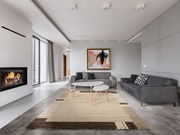 Moderner Wohnraum mit grauen Sofas, einem abstrakten Gemälde an der Wand und einem beigen Teppich mit geometrischem Muster auf dem Boden. Der Blick zeigt den Raum von vorne mit einem Kamin auf der linken Seite.