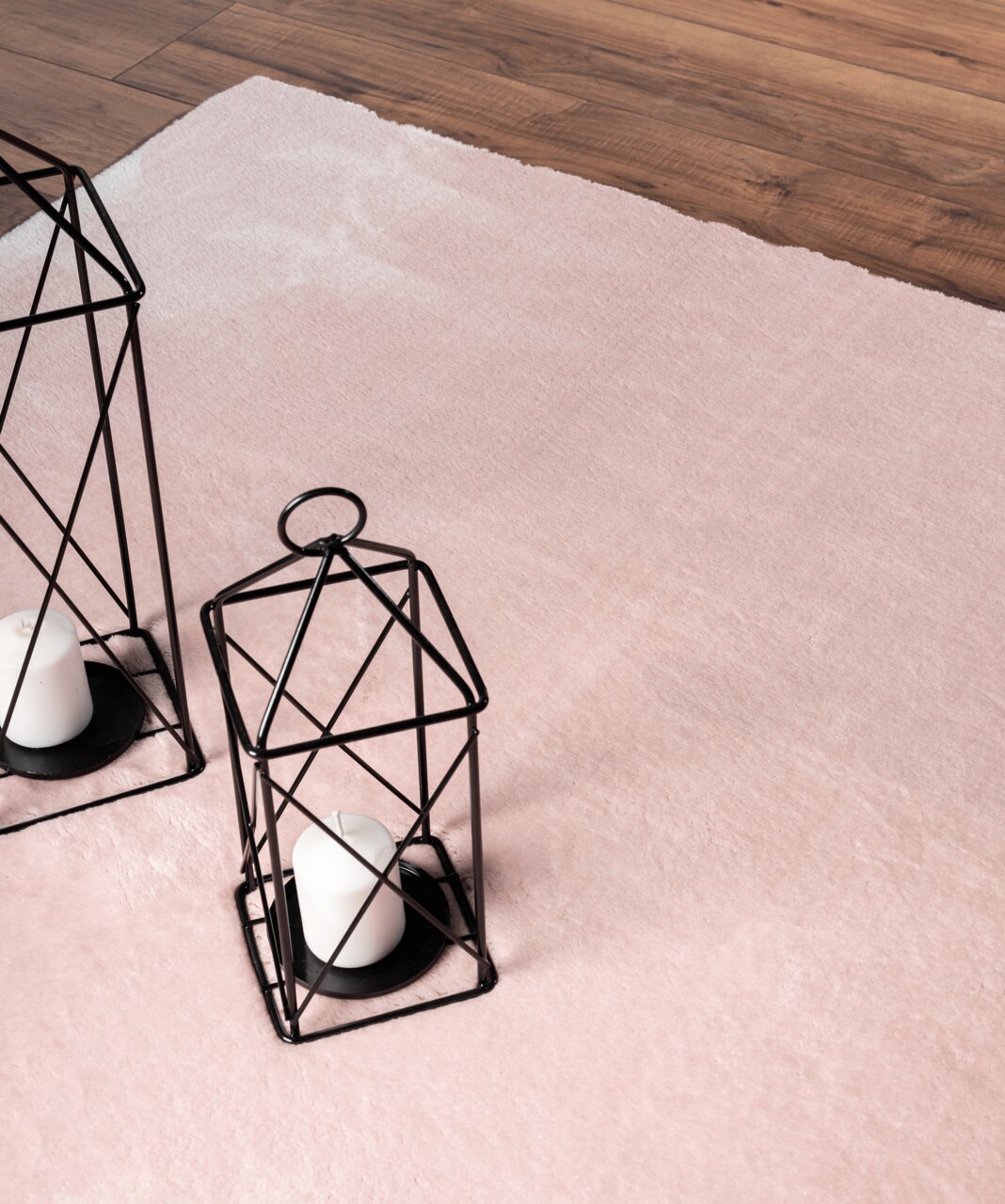 Roze tapijt Loft Rose, ca. 120 x 160 cm, op een houten vloer, met twee decoratieve zwarte lantaarns en witte kaarsen, gezien vanuit vogelperspectief.