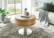 Moderne ronde houten salontafel met metalen onderstel, versierd met boeken en een vaas, in een gezellige woonkamer met tapijt en bank, gezien vanuit de zijkant.