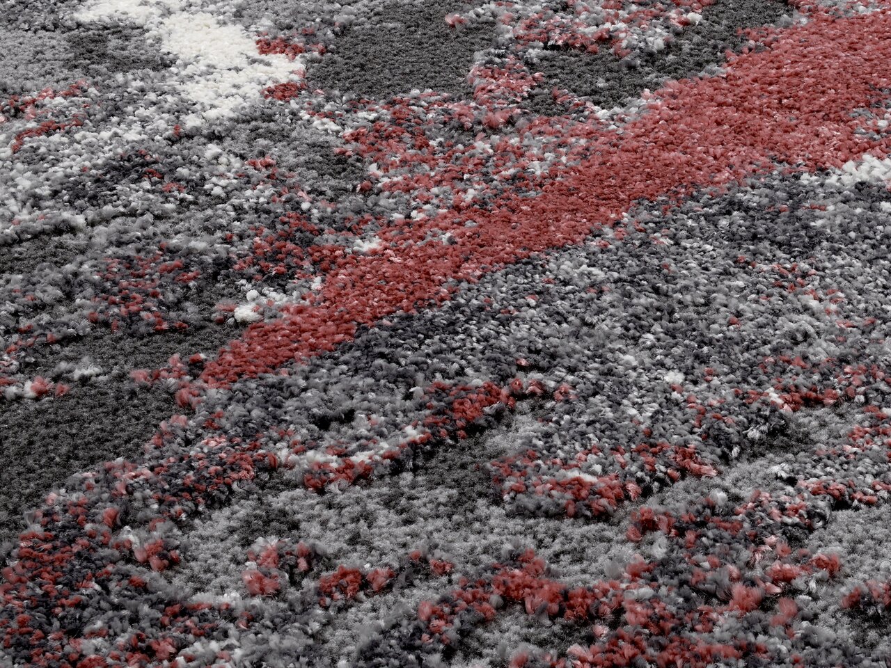 Nahaufnahme eines Designer-Teppichs mit abstraktem Muster in Grau-, Rot- und Weißtönen.