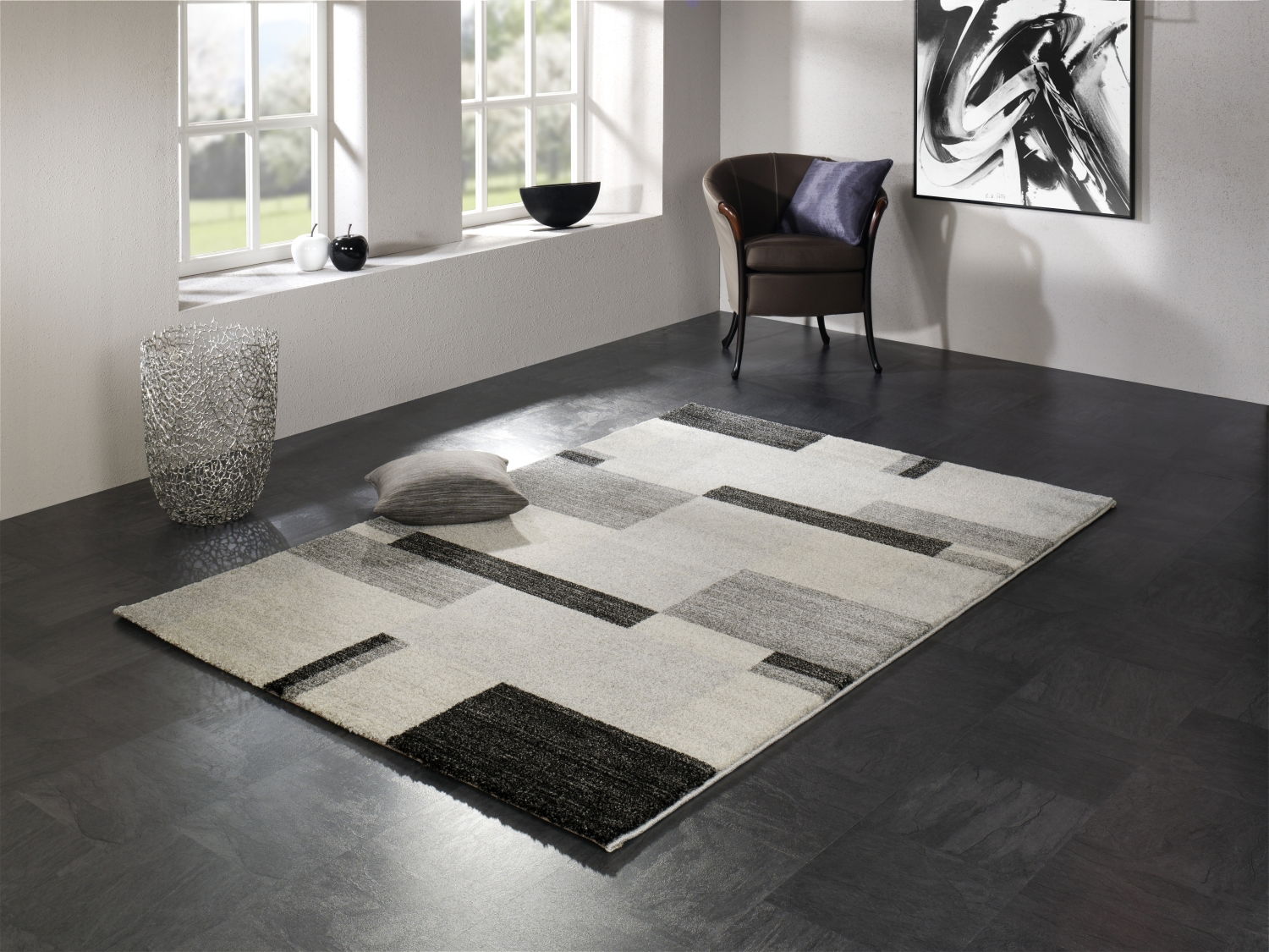 Moderner Teppich in Grau- und Schwarztönen mit geometrischem Muster, in einem stilvollen Raum mit Fenster, Sessel und Dekorationen, aus der Perspektive von schräg oben betrachtet.