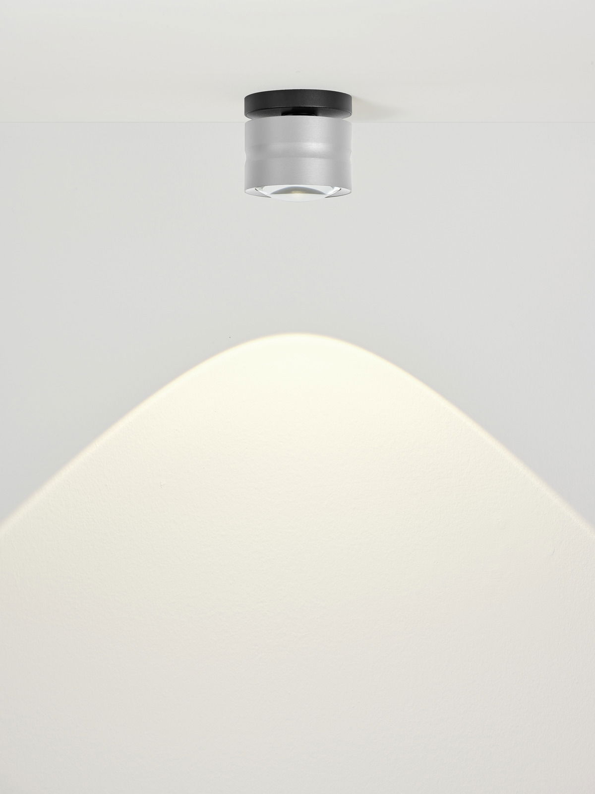 Moderne LED-Deckenleuchte MIKA in silberner Zylinderform, von unten betrachtet, mit sanftem Lichtkegel an der Decke.