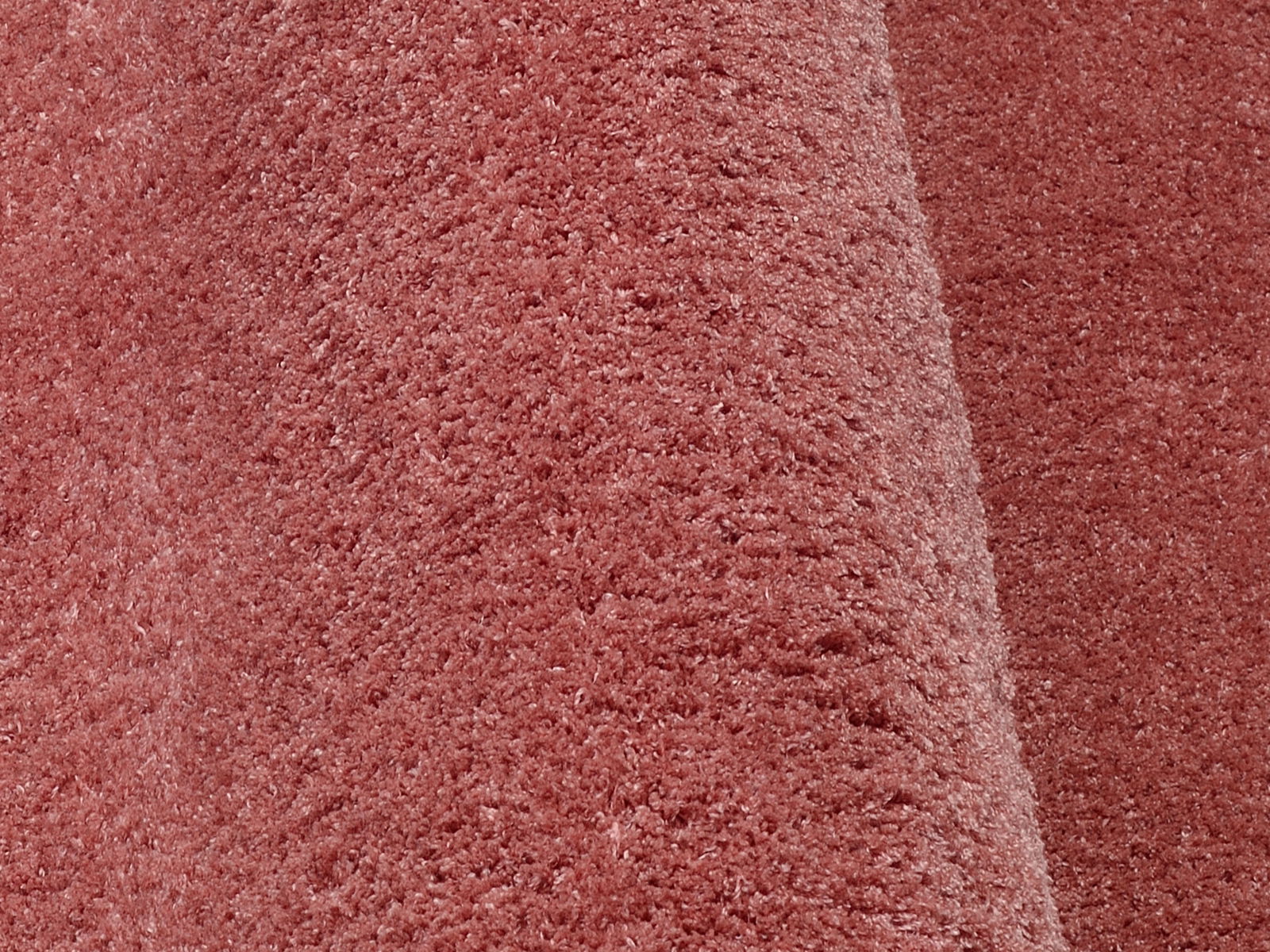 Nahaufnahme eines weichen, rosafarbenen Stoffes mit flauschiger Textur, perspektivisch von der Seite aufgenommen.