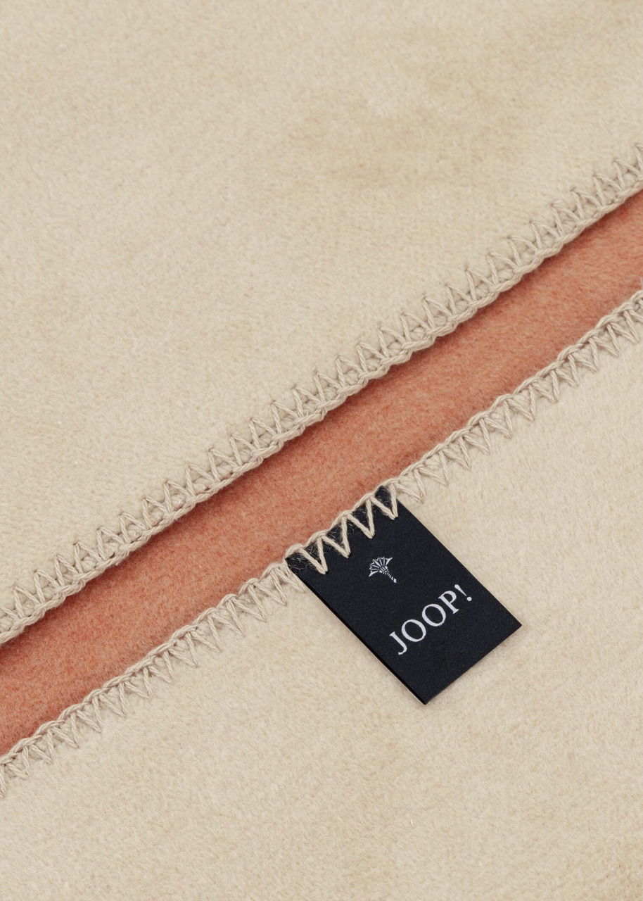 Nahaufnahme einer zweifarbigen Decke mit sichtbarem Joop-Label und Ziernaht.