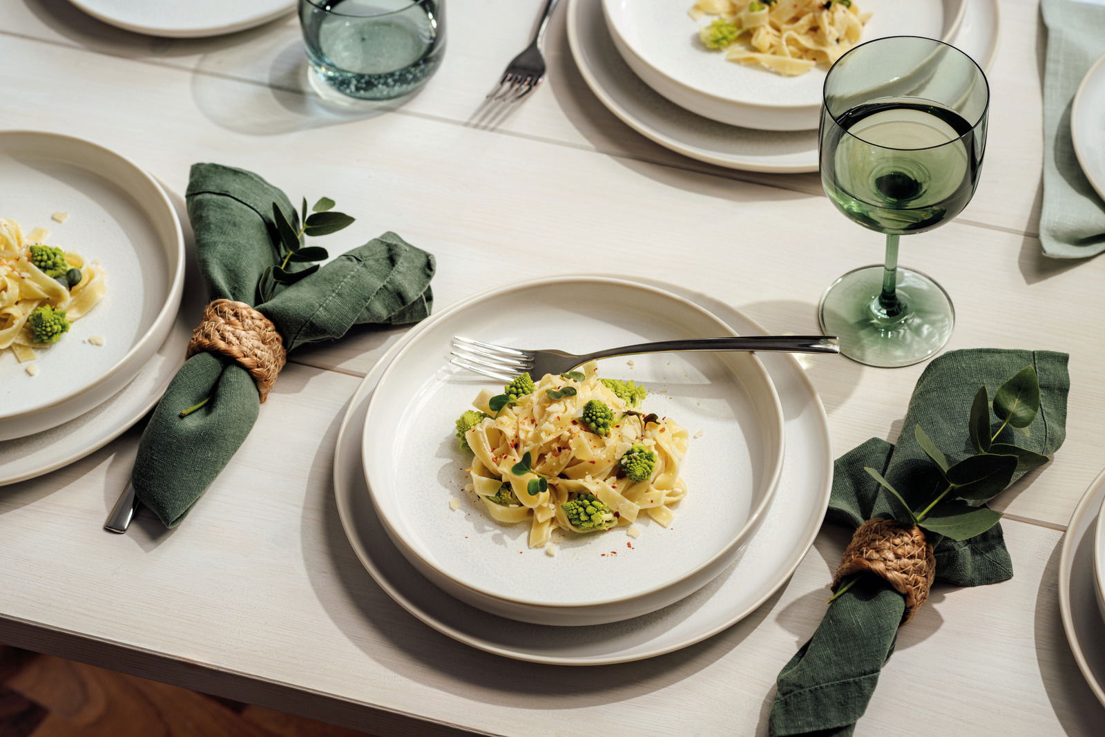 Elegantes Tafelset mit weißem Geschirr, grünen Servietten und Weingläsern, aus der Vogelperspektive fotografiert.