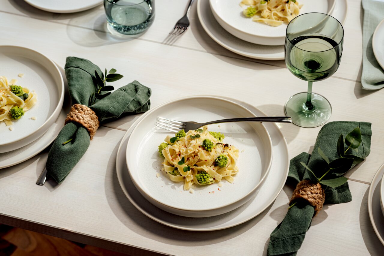 Elegantes Tafelset mit weißem Geschirr, grünen Servietten und Weingläsern, aus der Vogelperspektive fotografiert.