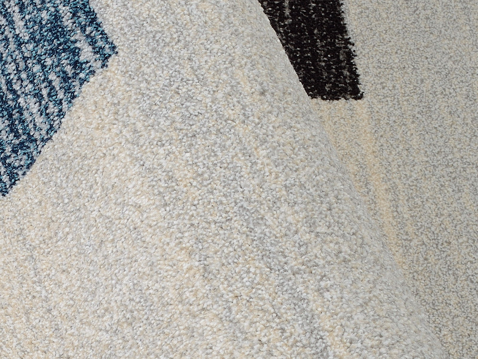 Nahaufnahme eines strukturierten Teppichs mit einem Muster in Blau- und Grautönen, perspektivisch von der Seite aufgenommen.