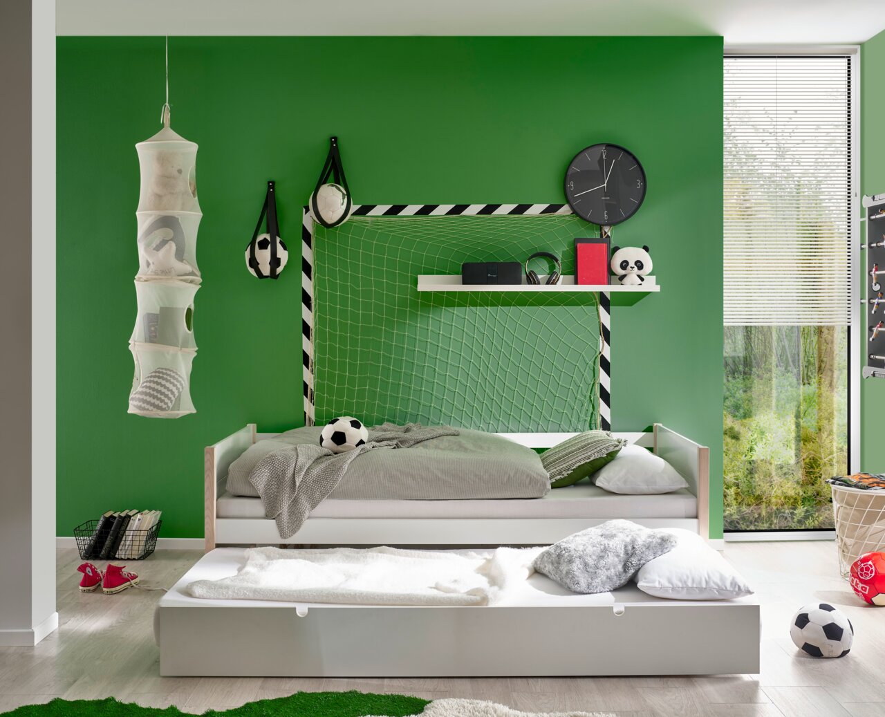 Jugendbett in einem Kinderzimmer mit grün gestrichener Wand, Fußball-Dekoration und einem ausziehbaren Bettkasten, seitliche Perspektive.