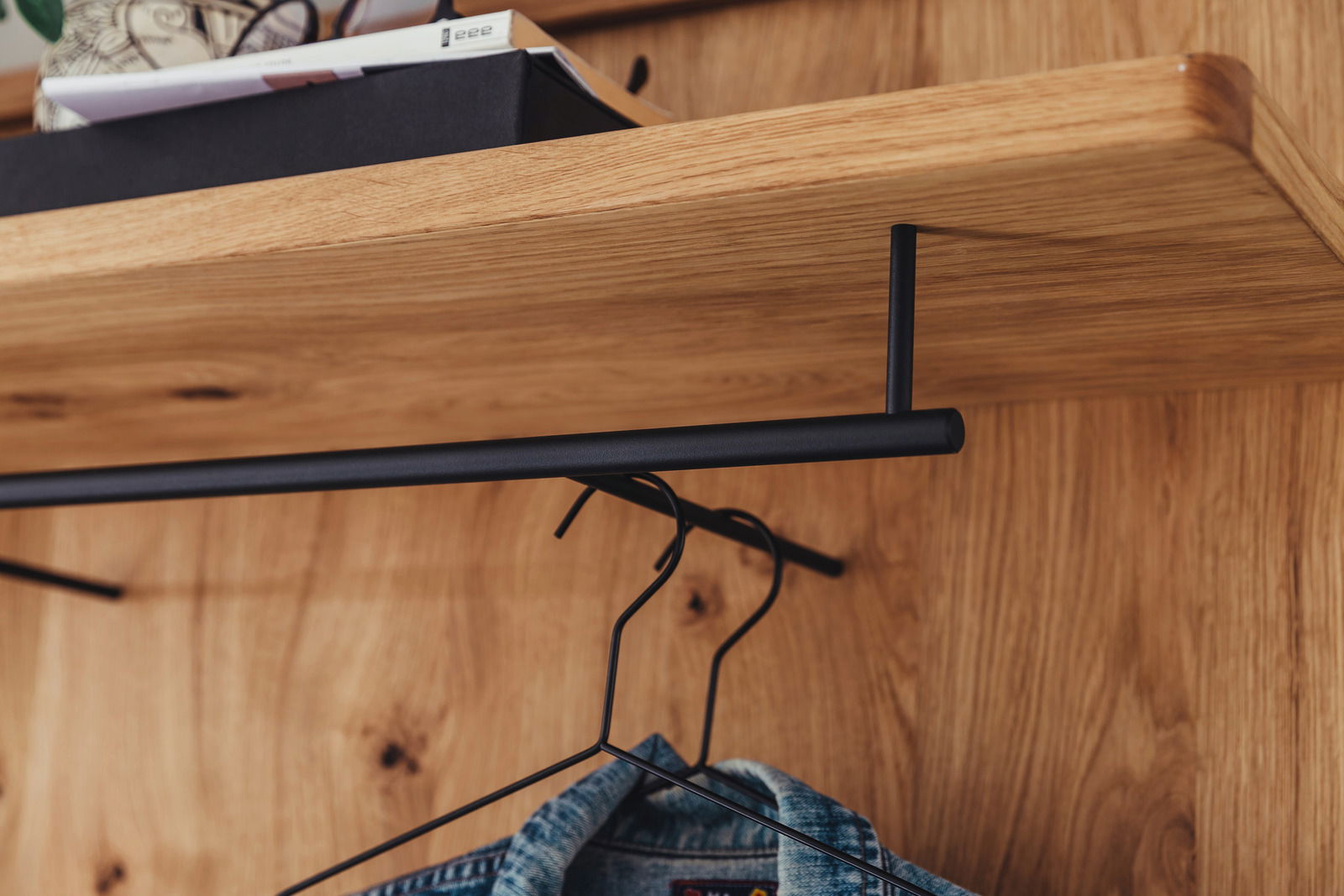 Nahaufnahme eines Garderobenpaneels aus Holz mit schwarzer Kleiderstange, von unten fotografiert.