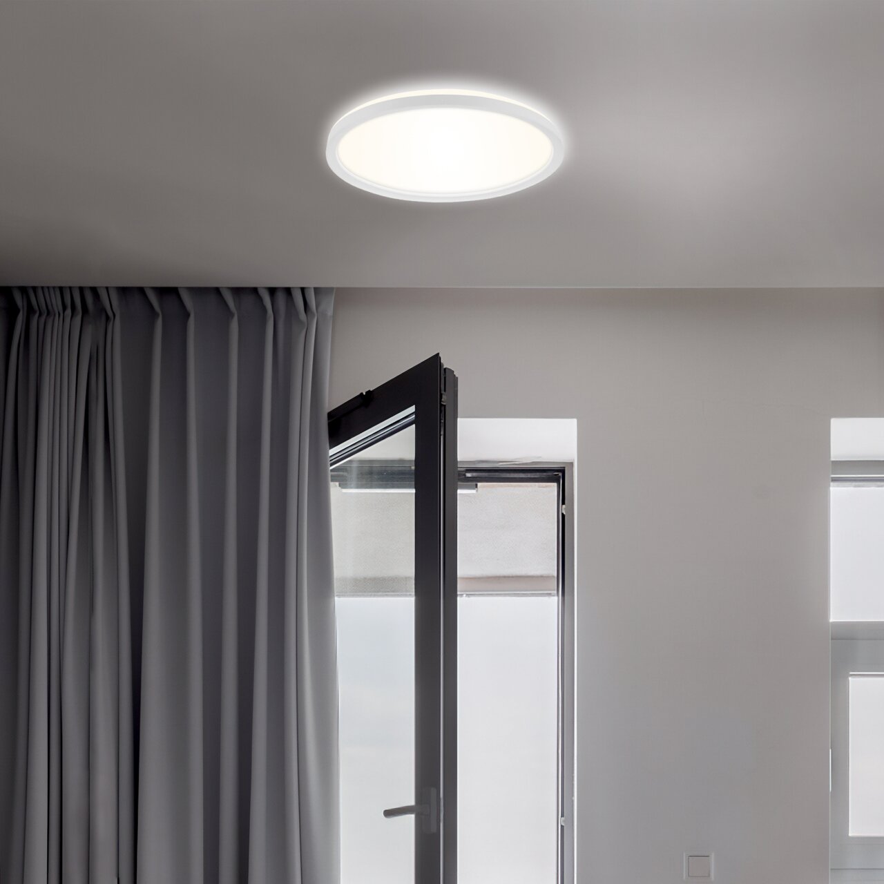 Moderne LED-Deckenleuchte Briloner SLIM, von unten betrachtet, in einem hellen Raum mit geöffnetem Fenster und Vorhängen.