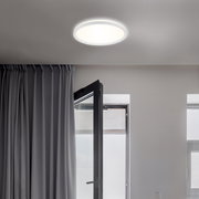Moderne LED-Deckenleuchte Briloner SLIM, von unten betrachtet, in einem hellen Raum mit geöffnetem Fenster und Vorhängen.