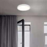 Moderne LED-Deckenleuchte Briloner SLIM, von unten betrachtet, in einem hellen Raum mit geöffnetem Fenster und Vorhängen.
