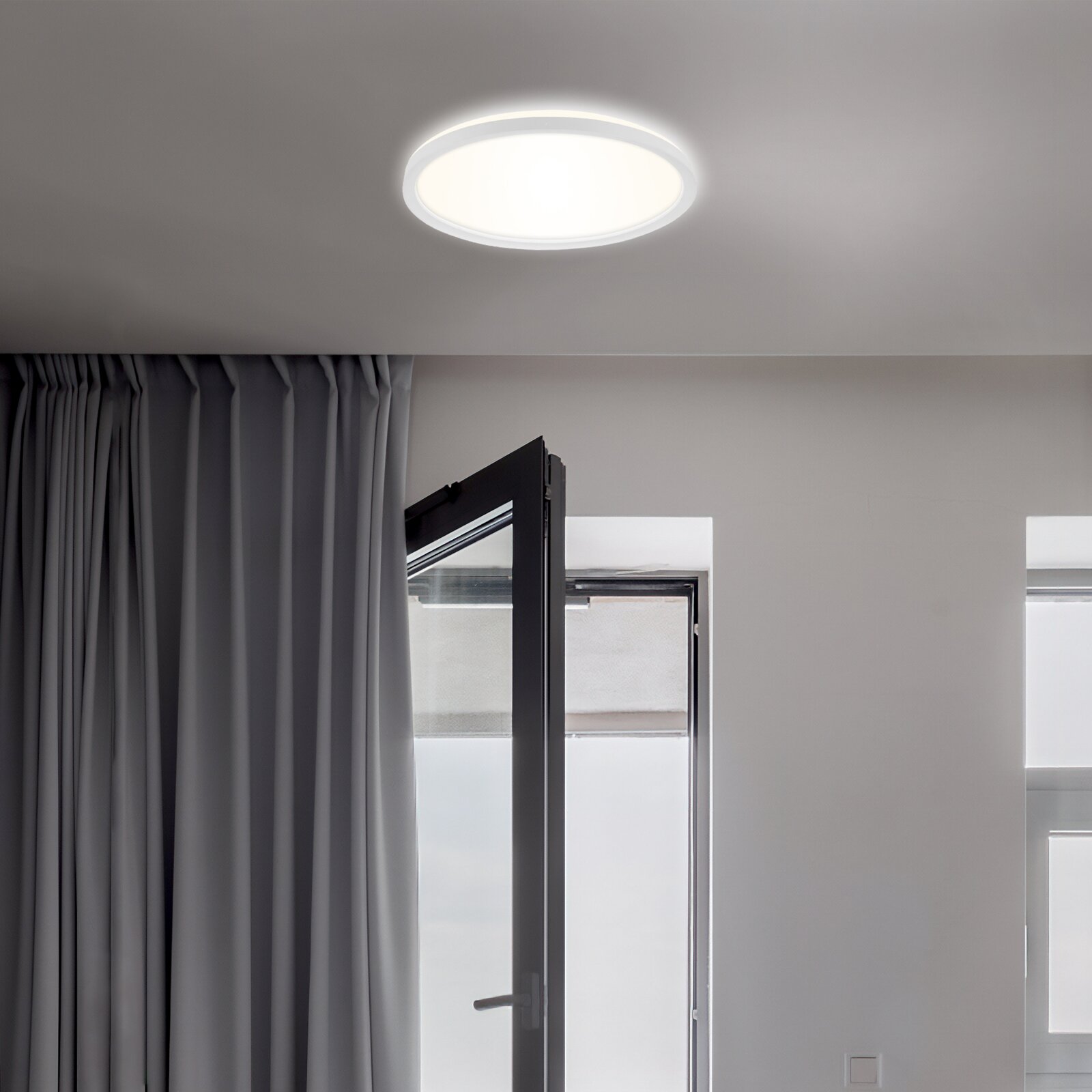 Moderne LED-Deckenleuchte Briloner SLIM, von unten betrachtet, in einem hellen Raum mit geöffnetem Fenster und Vorhängen.