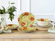 Blumenmuster-Geschirrset in Gelb mit orangefarbenen Blüten, Teller und Schalen dekorativ auf Holztisch arrangiert, perspektivisch in frontaler Tischansicht mit leicht schräger Seitenansicht