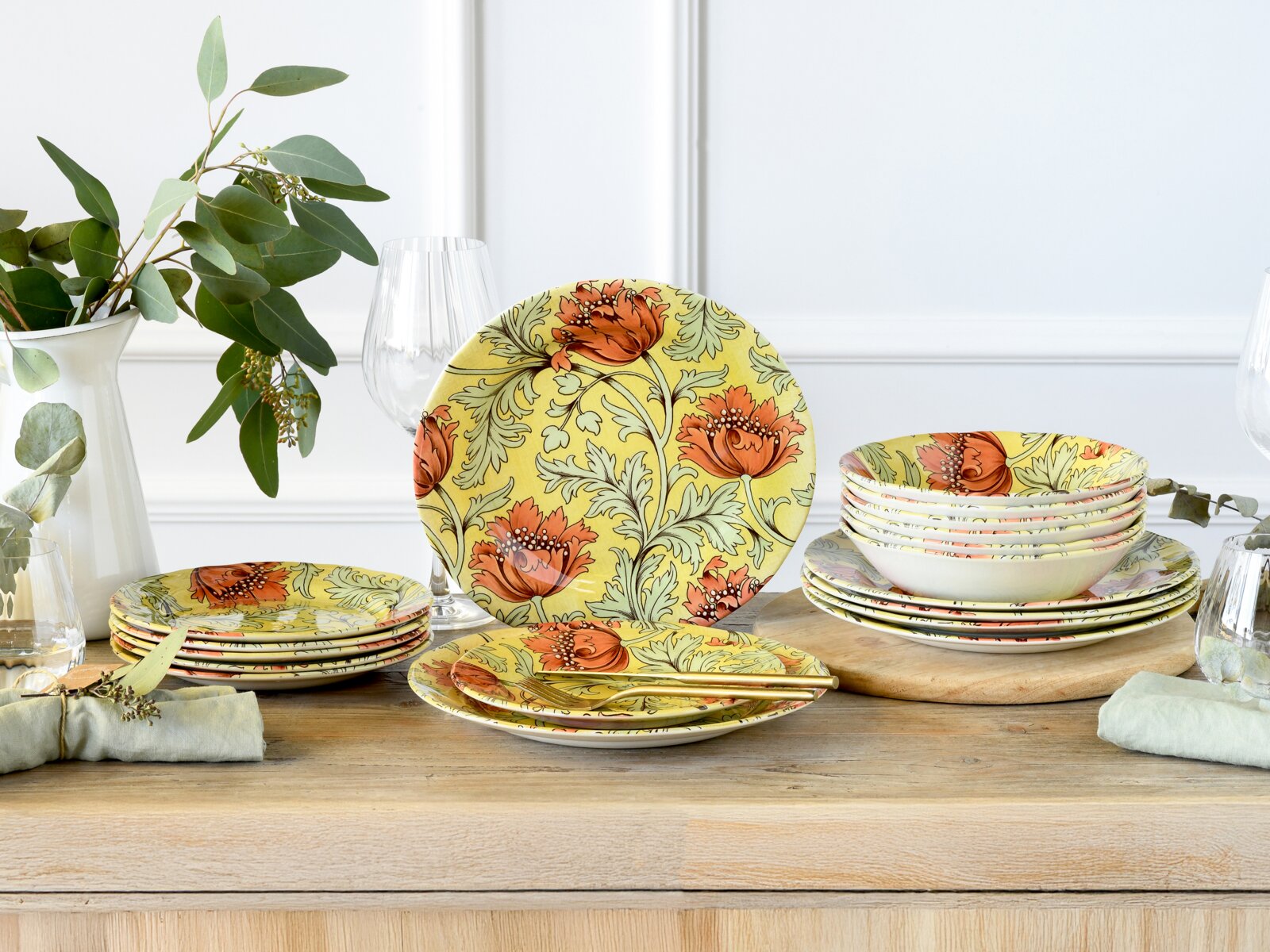 Blumenmuster-Geschirrset in Gelb mit orangefarbenen Blüten, Teller und Schalen dekorativ auf Holztisch arrangiert, perspektivisch in frontaler Tischansicht mit leicht schräger Seitenansicht