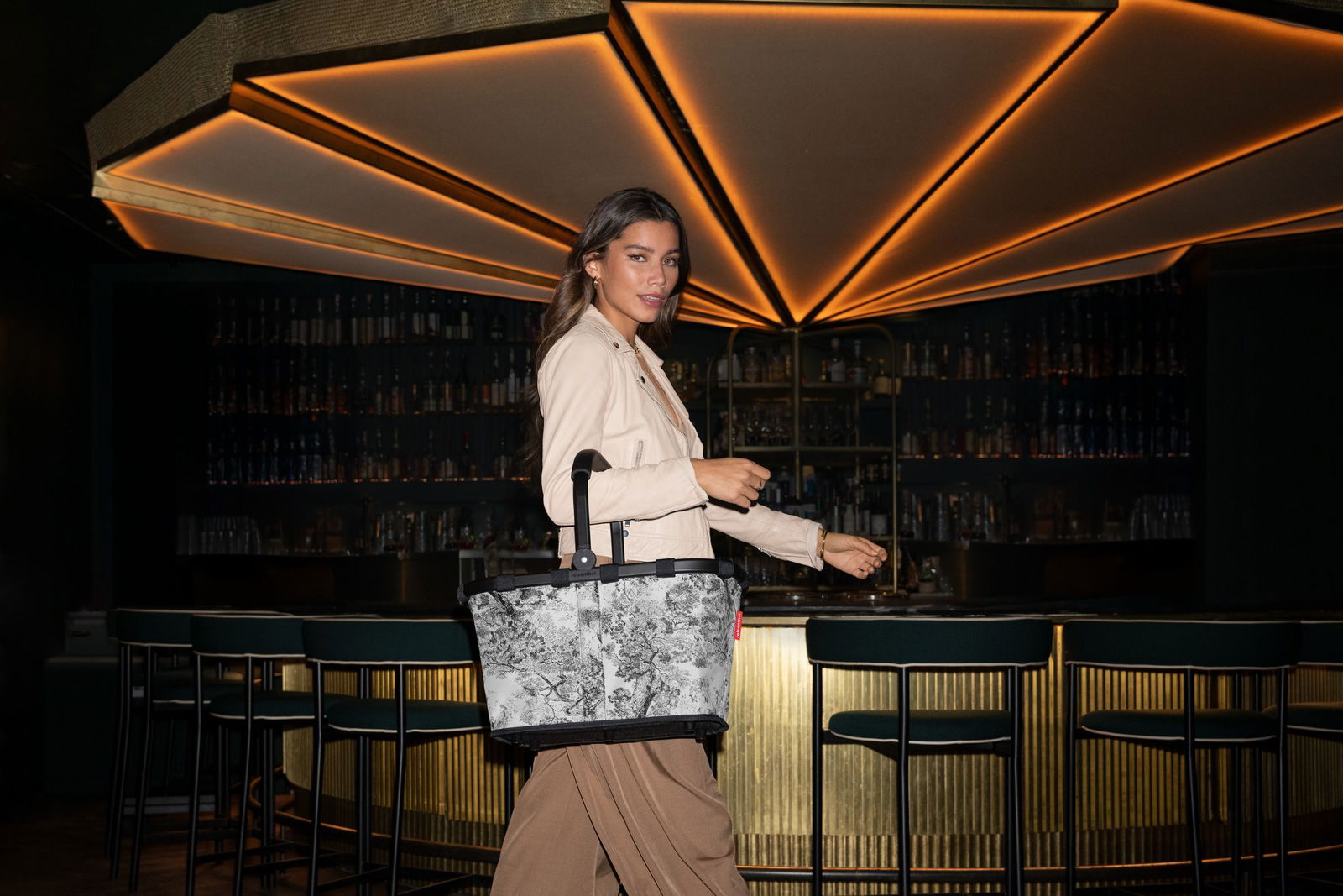 Frau mit stilvoller Tragetasche in einer eleganten Bar, seitliche Perspektive