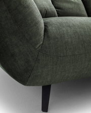Nahaufnahme eines dunkelgrünen Stoffsofas mit gepolsterter Armlehne, sichtbaren Nähten und schwarzem Metallfuß, seitliche Perspektive
