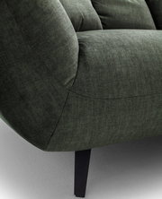 Nahaufnahme eines dunkelgrünen Stoffsofas mit gepolsterter Armlehne, sichtbaren Nähten und schwarzem Metallfuß, seitliche Perspektive