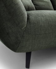Nahaufnahme eines dunkelgrünen Stoffsofas mit gepolsterter Armlehne, sichtbaren Nähten und schwarzem Metallfuß, seitliche Perspektive