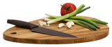 Schneidebrett in Tropfenform aus Akazienholz mit einem Messer, Frühlingszwiebeln, Knoblauchzehen und einer Tomate, seitliche Perspektive.