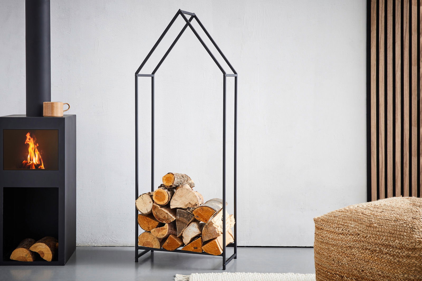 Moderner Kaminholzständer aus schwarzem Metall in Hausform, gefüllt mit Holzscheiten, seitliche Perspektive.