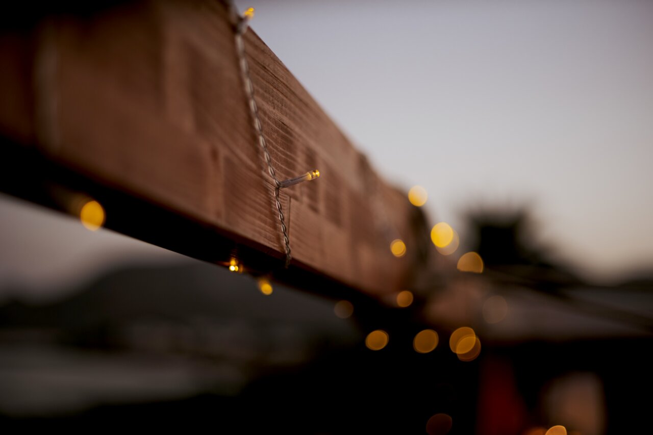 Close-up vanuit zijdelingse hoek van een lichtslinger met warmwitte leds, bevestigd aan een houten balk, met een onscherpe achtergrond in de schemering
