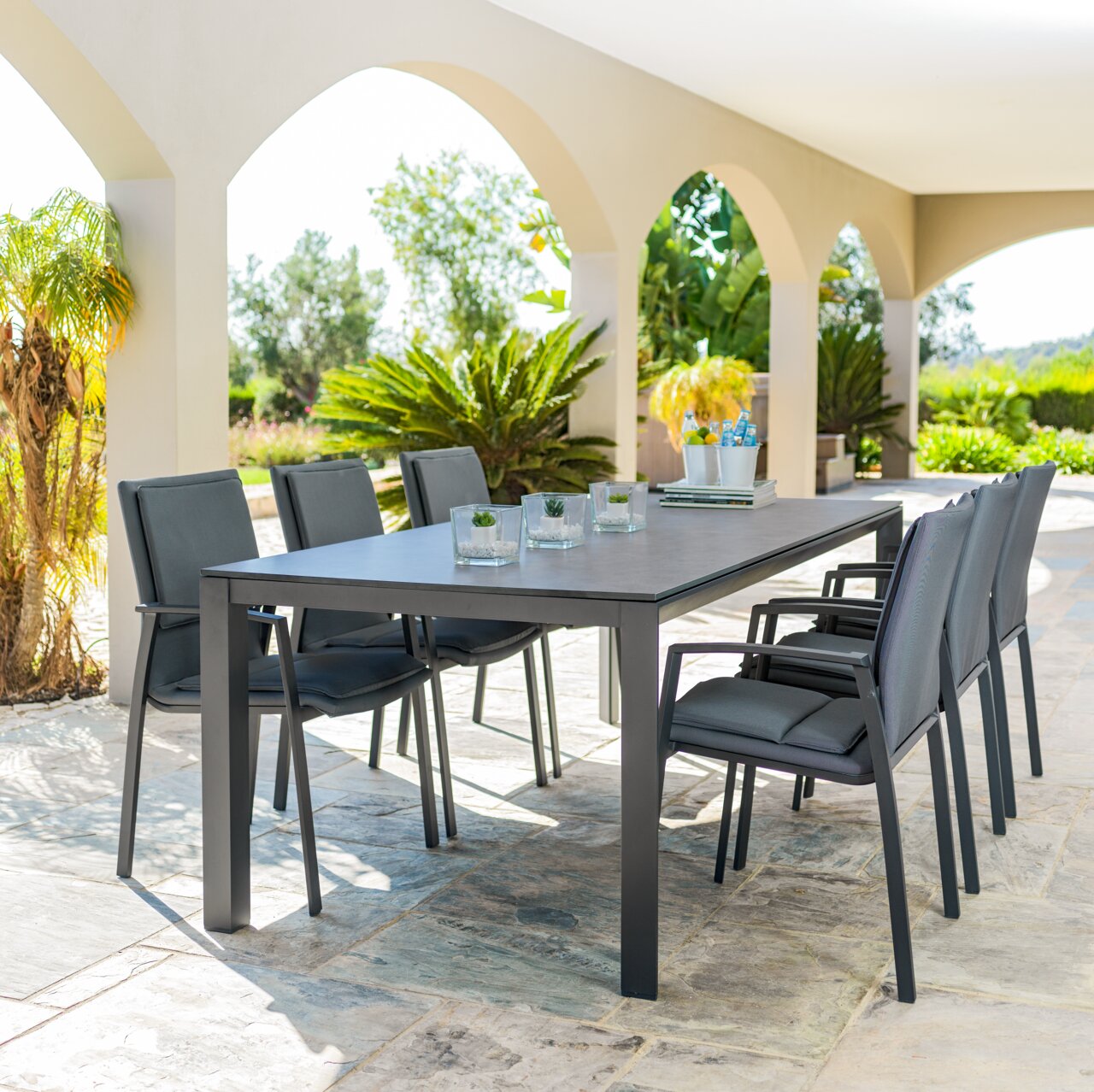 Moderne tuintafel met zes stoelen op een terras, omringd door planten, zijaanzicht.