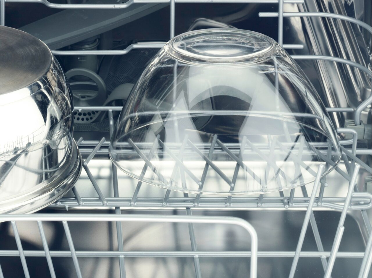 Binnenkant van een vaatwasser met een omgekeerd glas en een roestvrijstalen pan in de bovenste korf.
